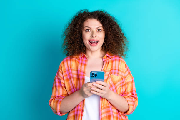 istock Young Woman Expressing Excitement While Holding Smartphone on Turquoise Background 2196441339