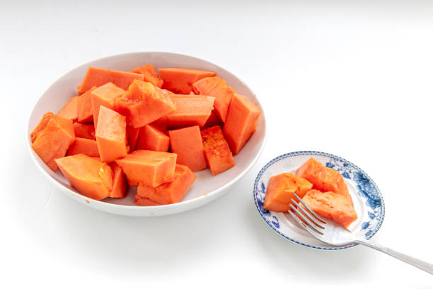 Sweet soft cut pieces of ripe papaya served on plates with a fork isolated on white.