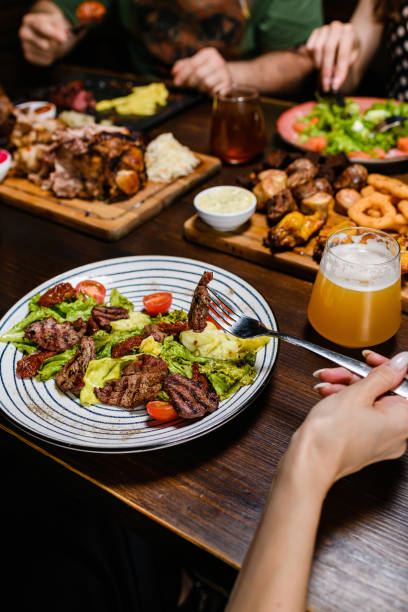 istock A person holds a fork with a bite, while beer and various dishes on a table. 2196445978