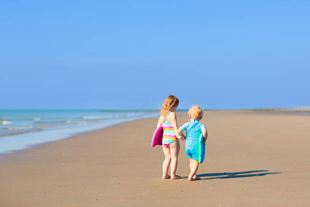 Kids playing on tropical beach. Water splash fun. Little boy splashing in sea waves. Children swim and play on summer family vacation. Sand and water toy, sun protection for young child.