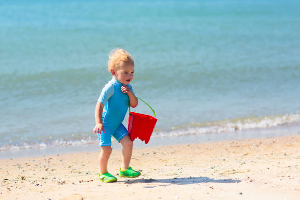 Kids playing on tropical beach. Water splash fun. Little boy splashing in sea waves. Children swim and play on summer family vacation. Sand and water toy, sun protection for young child.
