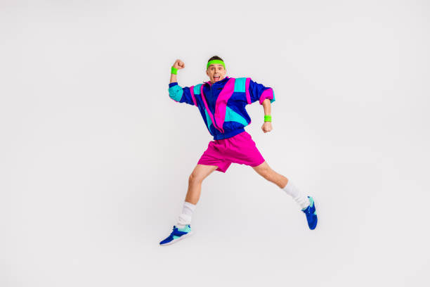 A young man in vibrant retro sportswear energetically jumps against a white background, showcasing fun, fitness, and a dynamic lifestyle.