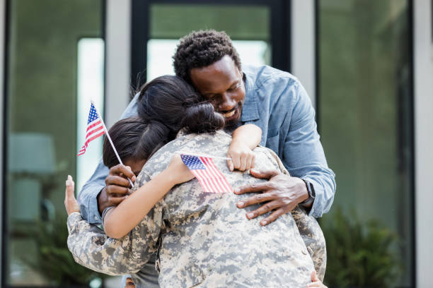 istock Family embraces returning soldier, holding small American flags 2196455468