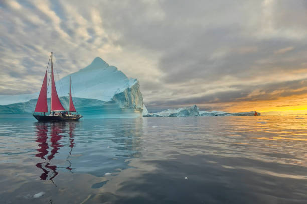 istock red sailboat sailing among floating icebergs in Disko Bay glacier with orange sunset during polar summer midnight solar season. Ilulissat, Greenland 2196457028