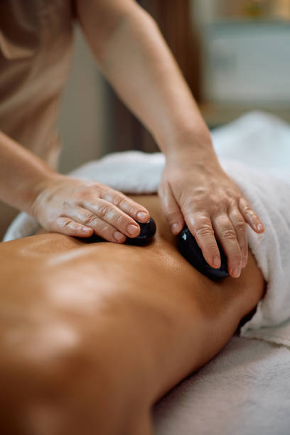 istock Close up of massage therapist using hot stones while massaging woman's back at health spa. 2196459613