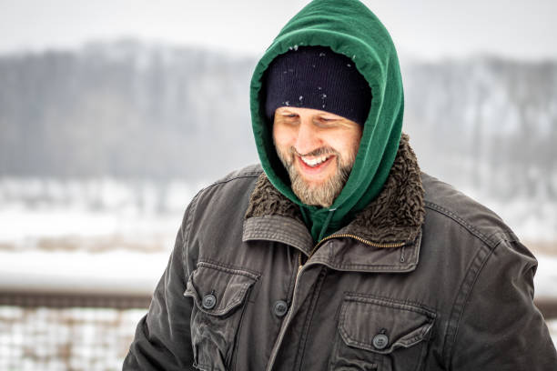 A close up of a man in winter clothing looking down and smiling , walking outside on a snowy Winter day