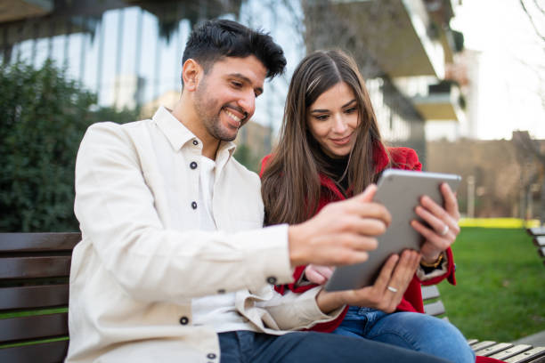 istock Young couple using digital tablet sitting on bench in the city 2196470294