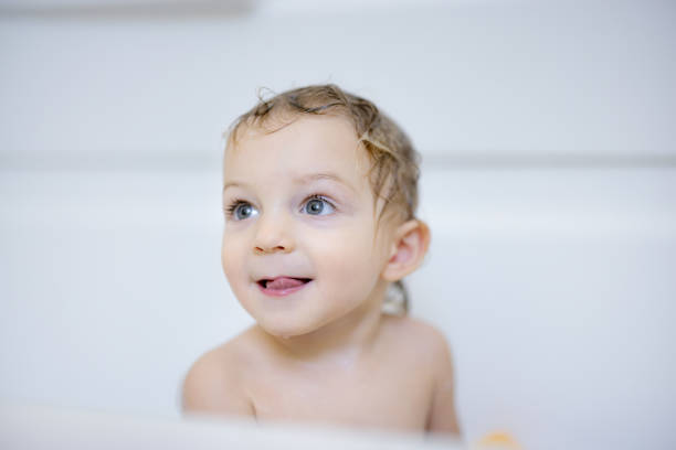 Little sweet girl takes bath with bath foam. Funny expression. Joy on face, smile.