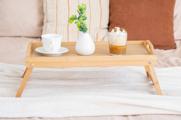 A simple wooden tray holds coffee and dessert by a vase with flowers on a bed.