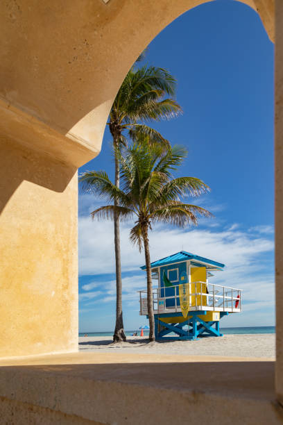 A classic architectural feature of Hollywood Beach, Florida, frames a colorful lifeguard tower in the background. This picturesque morning scene captures the charm of the beachfront, where Mediterranean-style elements blend seamlessly with the vibrant coastal atmosphere.