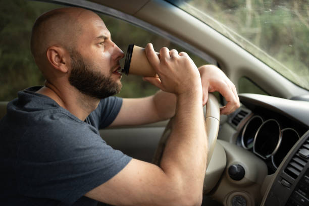 istock Millennial man drives a car and drinks coffee while holding the steering wheel 2196480745
