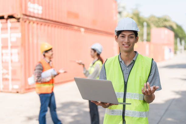istock Smiling construction engineer holding a laptop while coordinating with the team at a shipping container site 2196488999