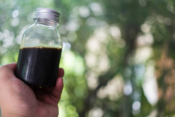 A hand holding round shape glass with black coffee against nature background