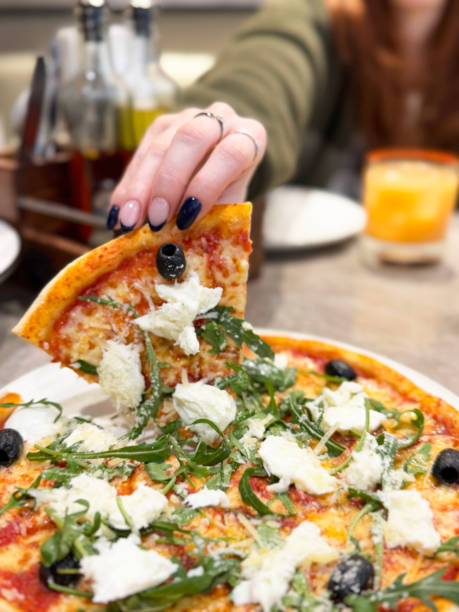istock Close-up image of unrecognisable redheaded woman holding thin, crispy crust burrata pizza slice being raised from plate, displaying French tip manicure, restaurant setting, focus on foreground 2196493802
