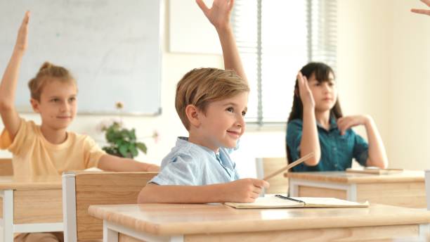 istock Smart caucasian boy raising hand for asking teacher at classroom. Pedagogy. 2196495362