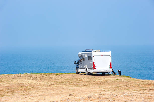 White camper van is parked on a sandy beach, with a calm blue ocean in the background, creating a serene and peaceful atmosphere