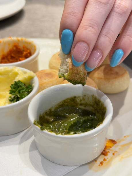 istock Full frame image of unrecognisable woman selecting bread sphere from white plate of fresh dough balls, ramekins of garlic butter garnished with parsley, red and green pesto, displaying blue French tip nail art, restaurant setting, focus on foreground 2196504511