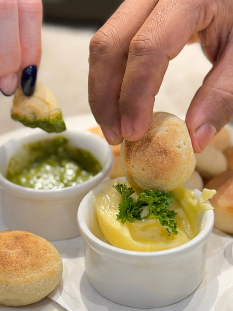 istock Full frame image of unrecognisable people dipping bread spheres from white plate of fresh dough balls into ramekins of garlic butter garnished with parsley and green pesto, displaying blue French tip nail art, restaurant setting, focus on foreground 2196504621