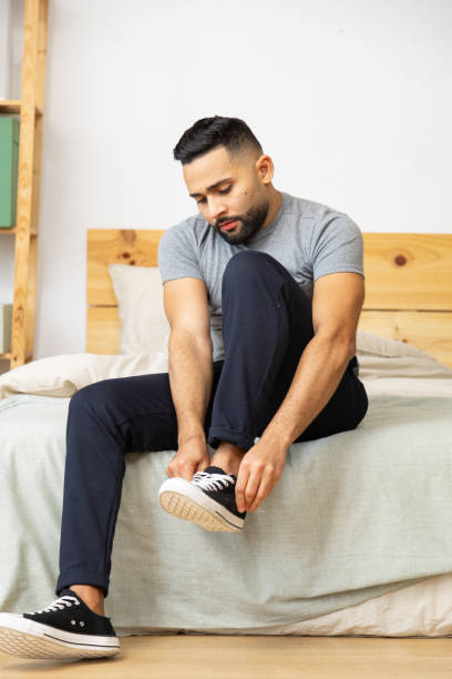 istock Young adult man tying sneakers on bed 2196521296