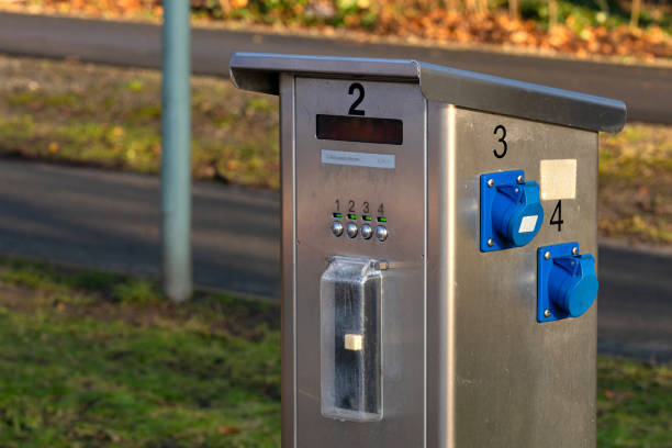 A sleek payment kiosk stands near a walking path in a public park. Visitors can use the interface to pay for park access. The setting features greenery and fallen leaves typical of autumn.