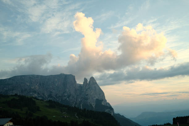The last rays of the setting sun are bathing the majestic peaks of the dolomites in a warm golden light, while dramatic clouds are floating across the sky