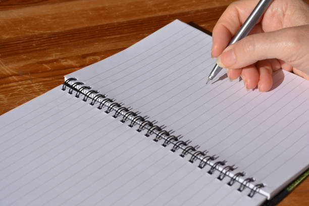 Spiral bound notebook opened to blank, lined page, with pen in hand poised to write