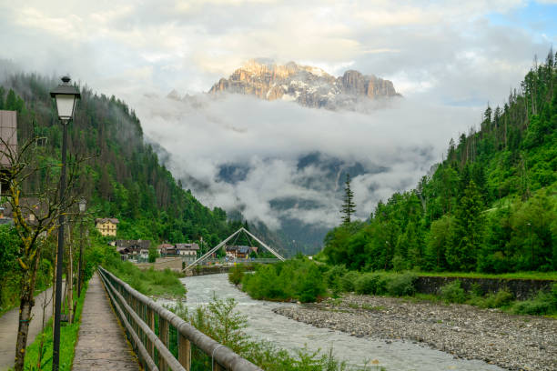 Monte Civetta mountain seen from the village Caprile along the Torrente Cordevole river in the Dolomites surrounded by clouds during sunset after a beautiful springtime day. The Civetta is a prominent and major mountain of the Dolomites, and is popular amongst mountaneers to climb as its one of the highest rock formations in Europe.