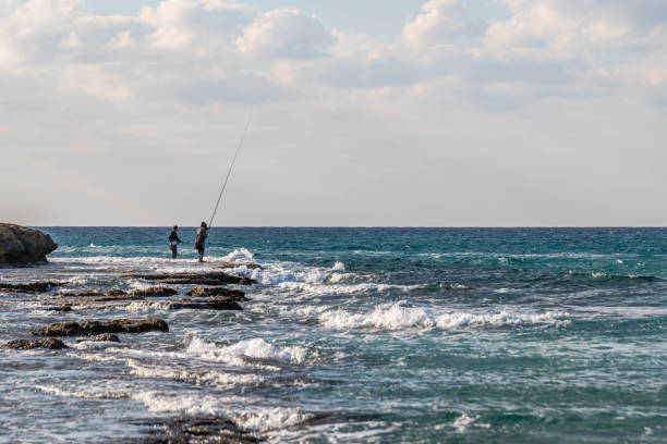 Two people fishing from the rocky coastline of HaBonim Beach in Israel.
