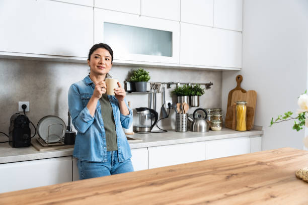 Young happy freshly divorced or recently single woman after toxic relationship breakup standing at kitchen in new apartment she rent drinking coffee or tea enjoying new beginnings and morning silence