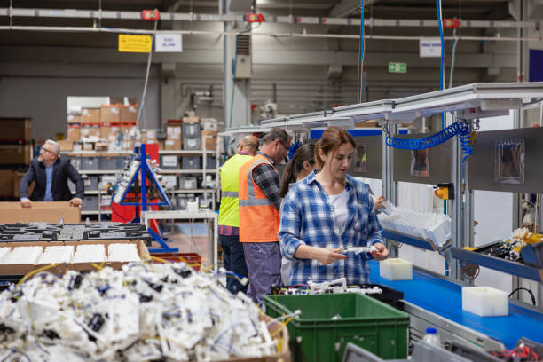 Concentrated professional young industrial factory workers working with machine parts hands using electric pneumatic screwdriver retractable mechanism, fastened with screws in large Electric electronics wire and cable manufacturing plant factory warehouse.