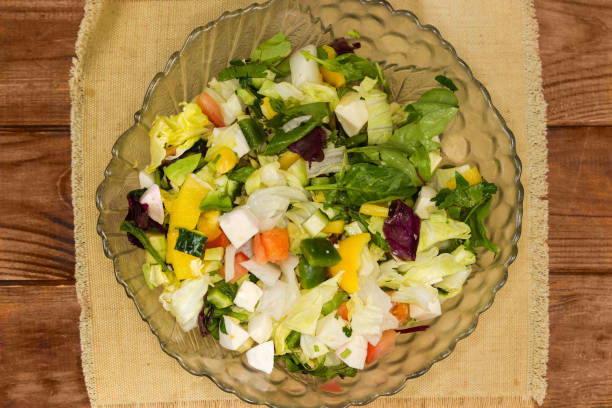 Salad of mozzarella, avocado, different fresh vegetables and leaf lettuce in a glass salad bowl on a rustic table, top view