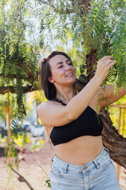 istock A happy woman is standing under a tree touching the leafs and smiling 2196543777