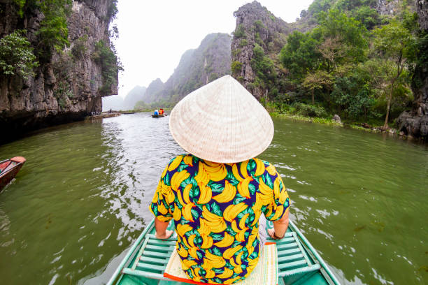 istock Tourist wearing a traditional vietnamese conical hat navigating Tam Coc river in Ninh Binh, Vietnam 2196571738