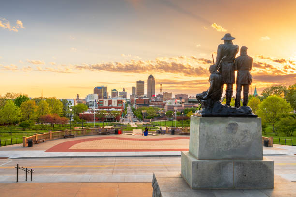 Des Moines, Iowa, USA - May 3, 2024: The Pioneer Statuary Group on the Iowa State Capitol grounds with the Des Moines skyline in the distance at dusk.