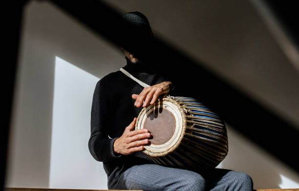 istock Close of man hands in black clothes, sitting and having joy while playing mridangam, an ancient percussion musical instrument originating from the Indian subcontinent in sunny day inside. Copy space 2196581425
