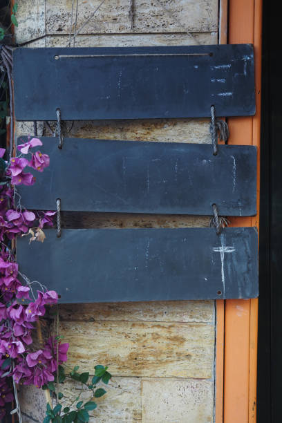 A clean, blank chalkboard sign hangs elegantly among decorative vines on a stone wall