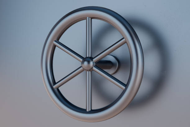A silver metal wheel with six spokes. The wheel is in a room with a gray wall. The wheel is not in motion