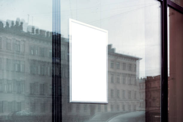 Glass window reflecting urban streetscape behind vertical white poster, creating layered visual depth for graphic design and marketing presentations