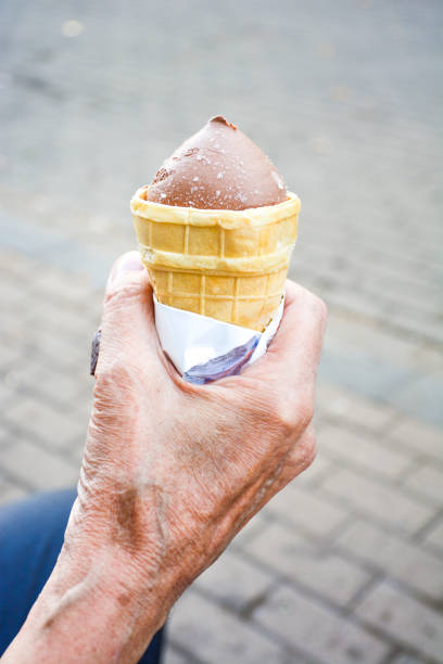 This is a photograph with a shallow depth of field of ice cream cone being held up against a New York City Street on a hot sunny day.