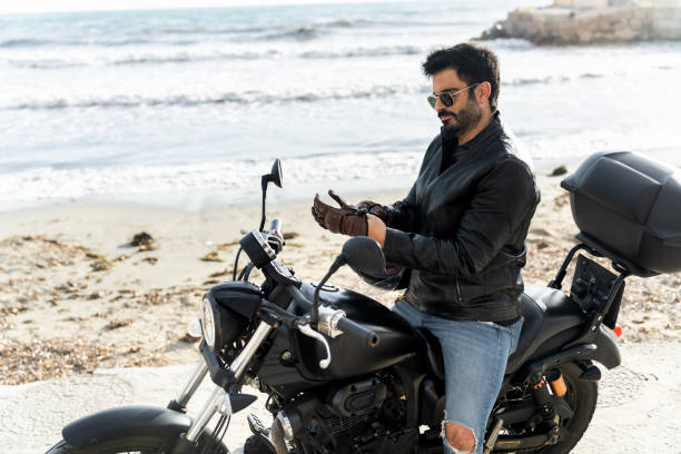 istock Biker wearing leather jacket putting gloves on his motorcycle on the beach 2196591351