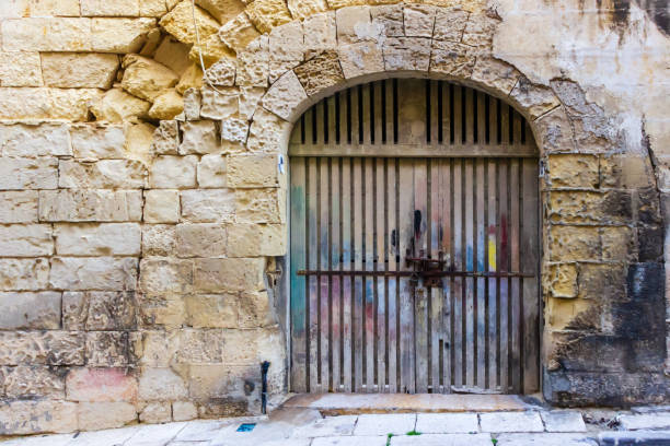 Rugged stone wall featuring an arched rusty metal gate, with vibrant traces of colorful graffiti adding urban character, representing vintage charm, history, and an urban texture in an evocative street environment.