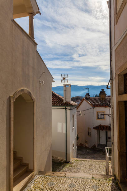 istock A narrow cobblestone pathway between buildings offers a glimpse of a distant misty landscape under a partly cloudy sky. 2196598871