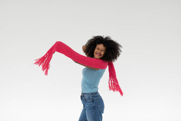 A joyful woman playfully showcasing a vibrant pink scarf around her neck while wearing a fitted blue top and denim jeans, radiating warmth and happiness.