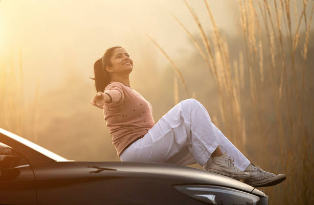 istock Smiling woman sitting on car hood during weekend at sunset 2196602871