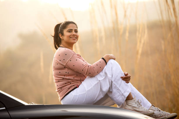 istock Smiling woman sitting on car hood during weekend at sunset 2196602903
