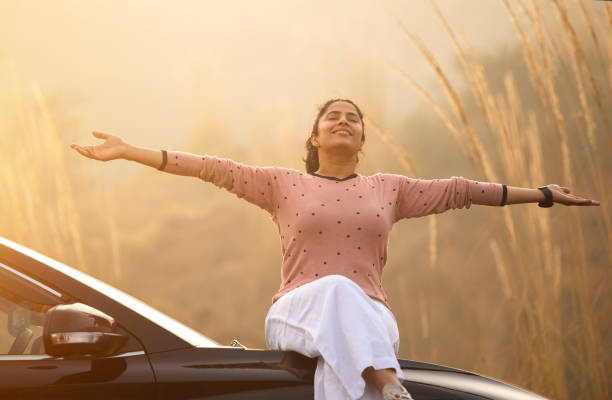 istock Smiling woman sitting on car hood during weekend at sunset 2196604178
