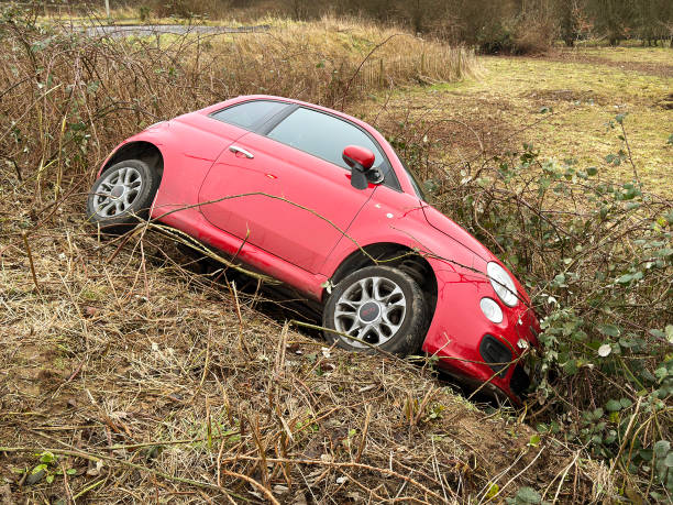 Pontyclun, Wales, UK - 29 January 2025: Small red car on its side in bushes after crashing off a road. No people.