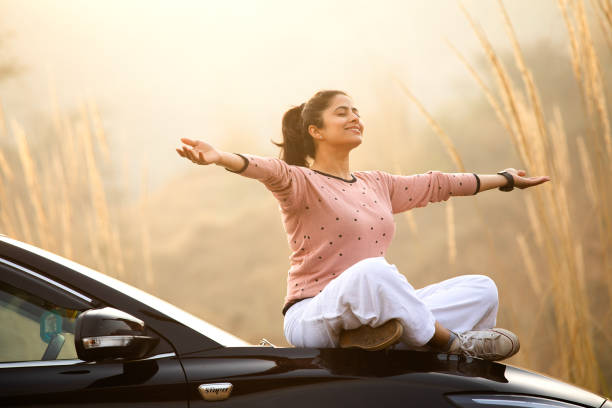 Smiling woman with arms outstretched sitting on car