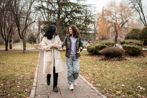 istock Two girls walking and talking in the park 2196610913