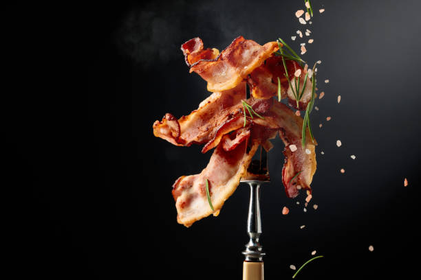 istock Fried bacon on a fork, sprinkled with rosemary and pink salt. 2196616494